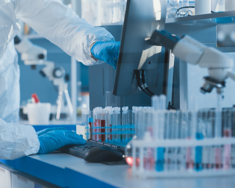 Scientist's gloved hand pointing at radiochemistry results on a computer